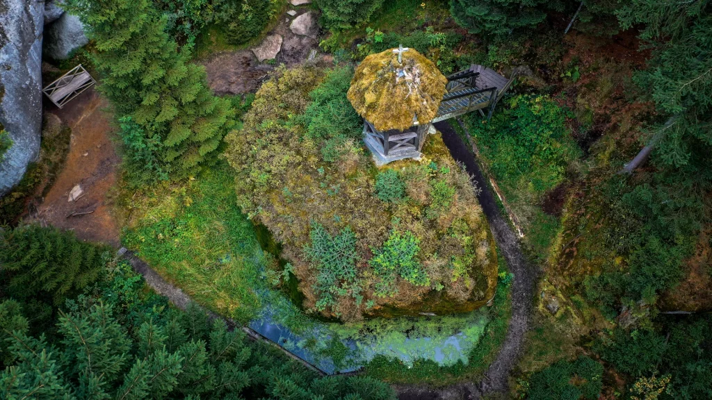 Luftaufnahme eines kleines AUssichtshaus auf einer Felseninsel. Um den Felsen herum ist Wasser erkennbar und viel Grün.