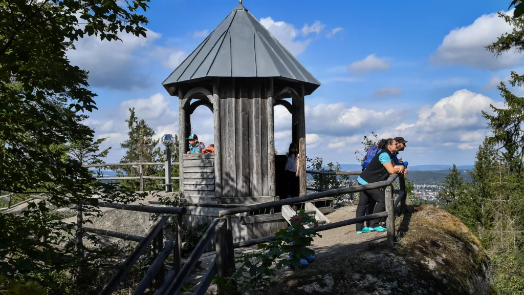 Eine Aussichtsplattform im Felsenlabyrinth. Rechts stehen zwei erwachsene am Geländer und blicken in die Ferne.